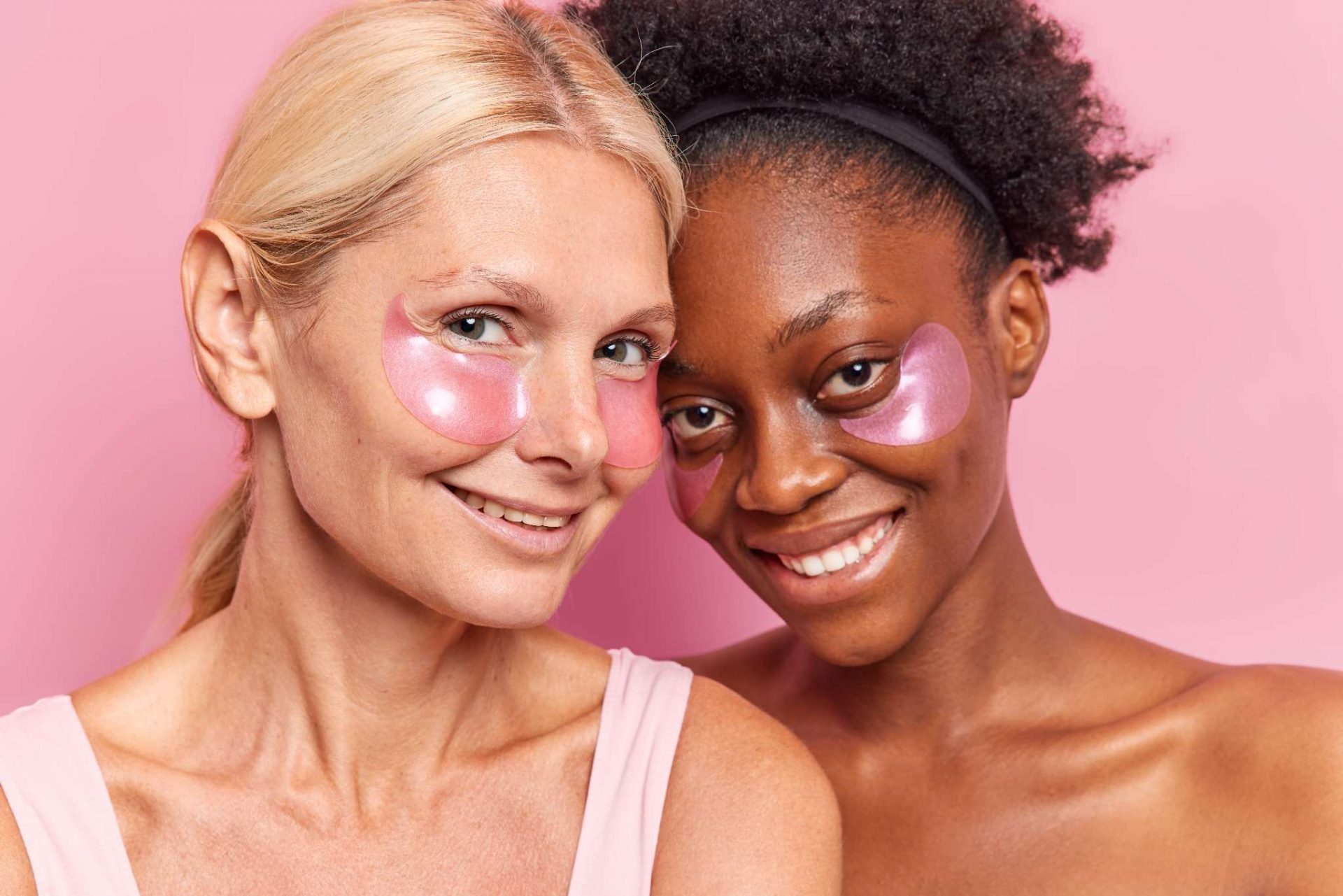 Deux femmes souriantes portent des patchs contour des yeux hydratants pour préparer la peau avant l’application d’un anti-cernes illuminateur.
